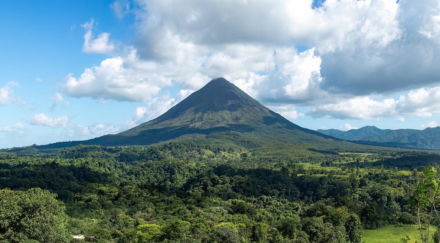 Arenal Volcano's cone rising above dense green rainforest under a blue sky