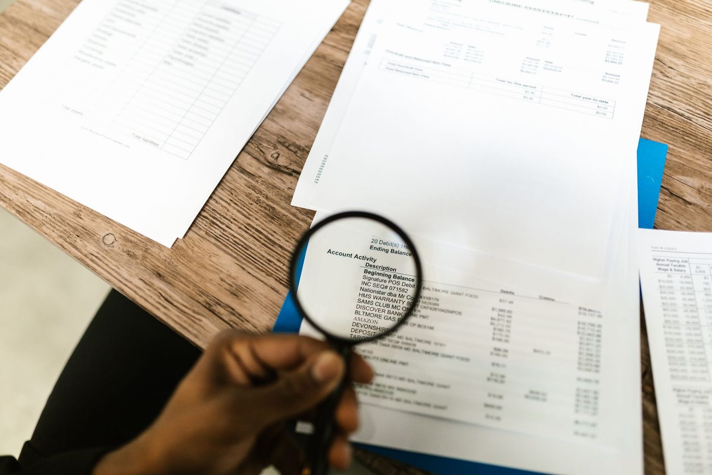 Hand holding a magnifying glass over a financial statement on a desk