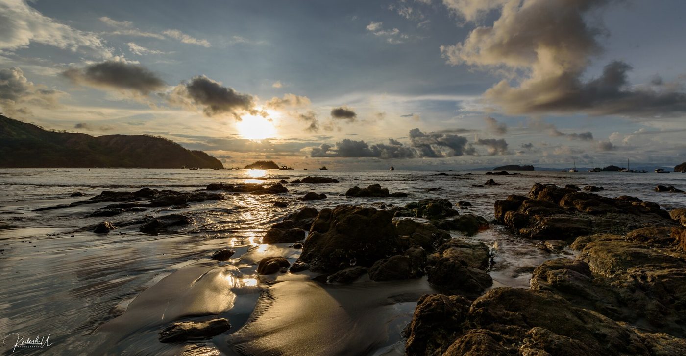 Sunset over Playas del Coco bay with wet sand reflections and anchored boats