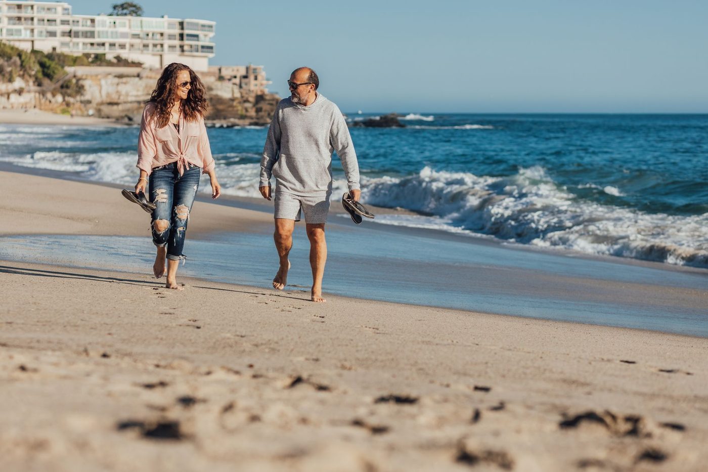 Retired couple walking barefoot along the shoreline on a sunny morning