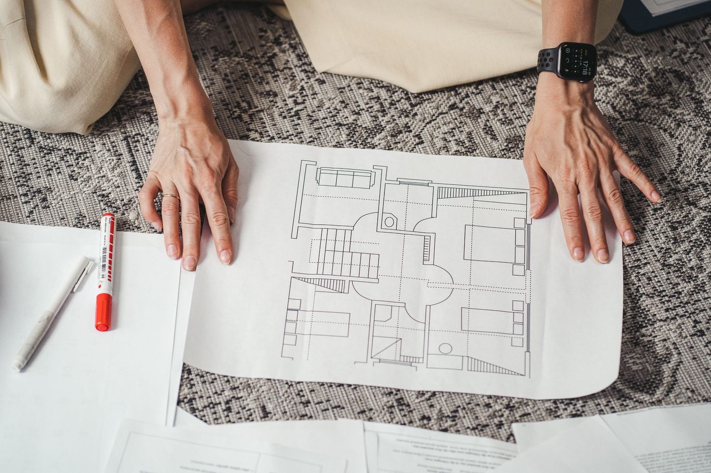 Hands reviewing a printed house floor plan alongside permit documents on a table