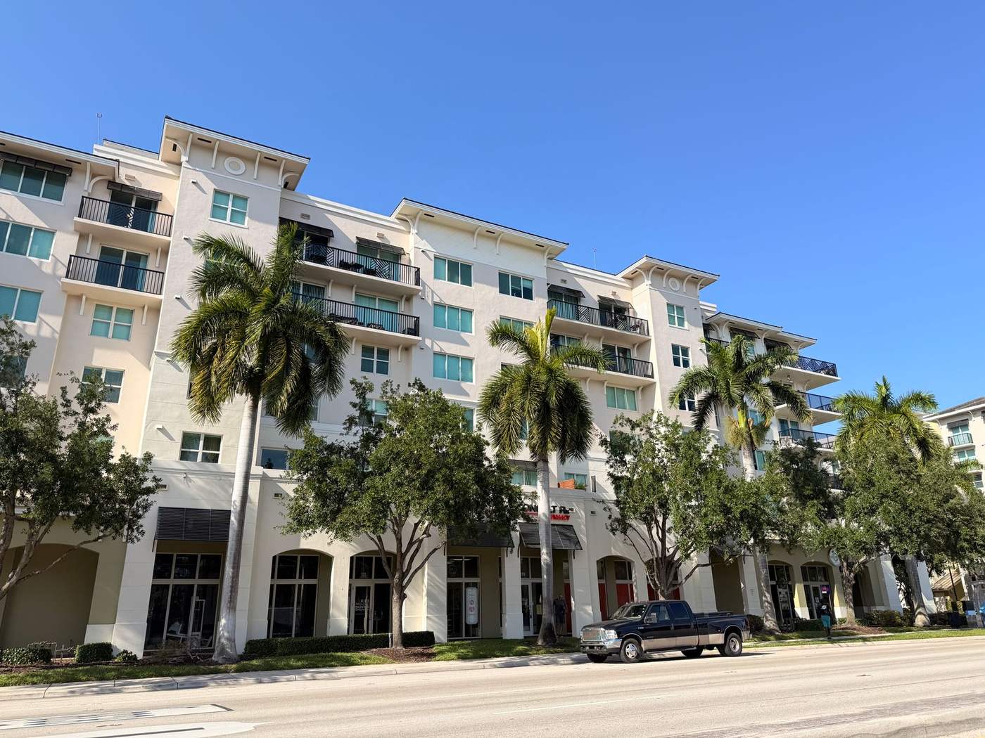 Multi-story condominium building with palm trees and street-level shops below