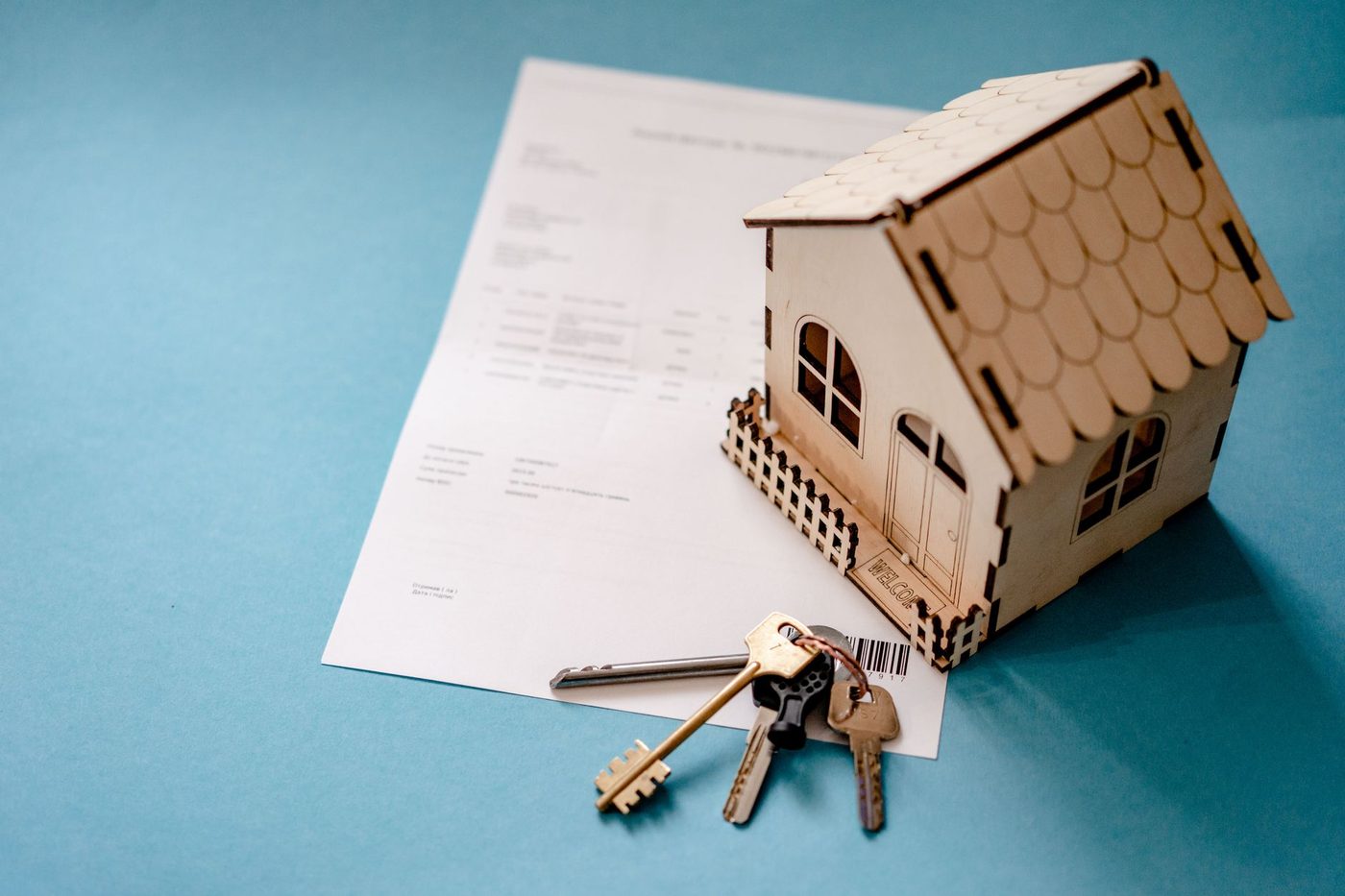 Small wooden house model with keys resting on a sale contract