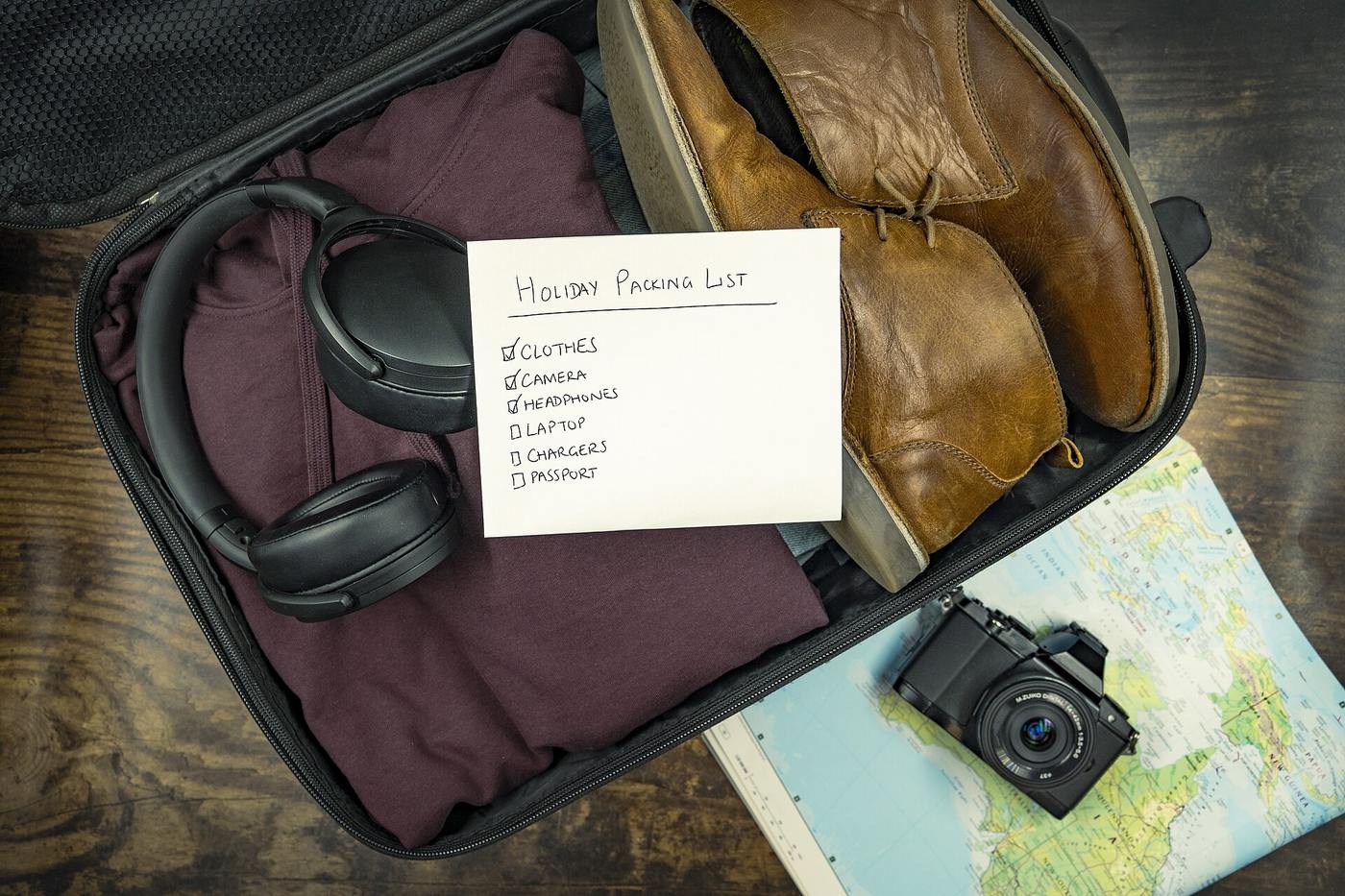 Open suitcase with handwritten holiday packing list, boots, headphones and camera