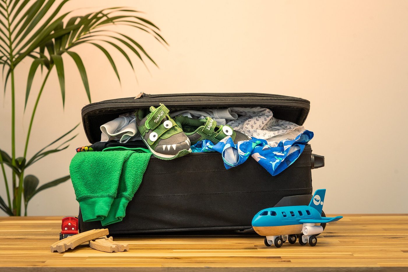 Overstuffed suitcase spilling swim trunks and shoes beside a palm plant