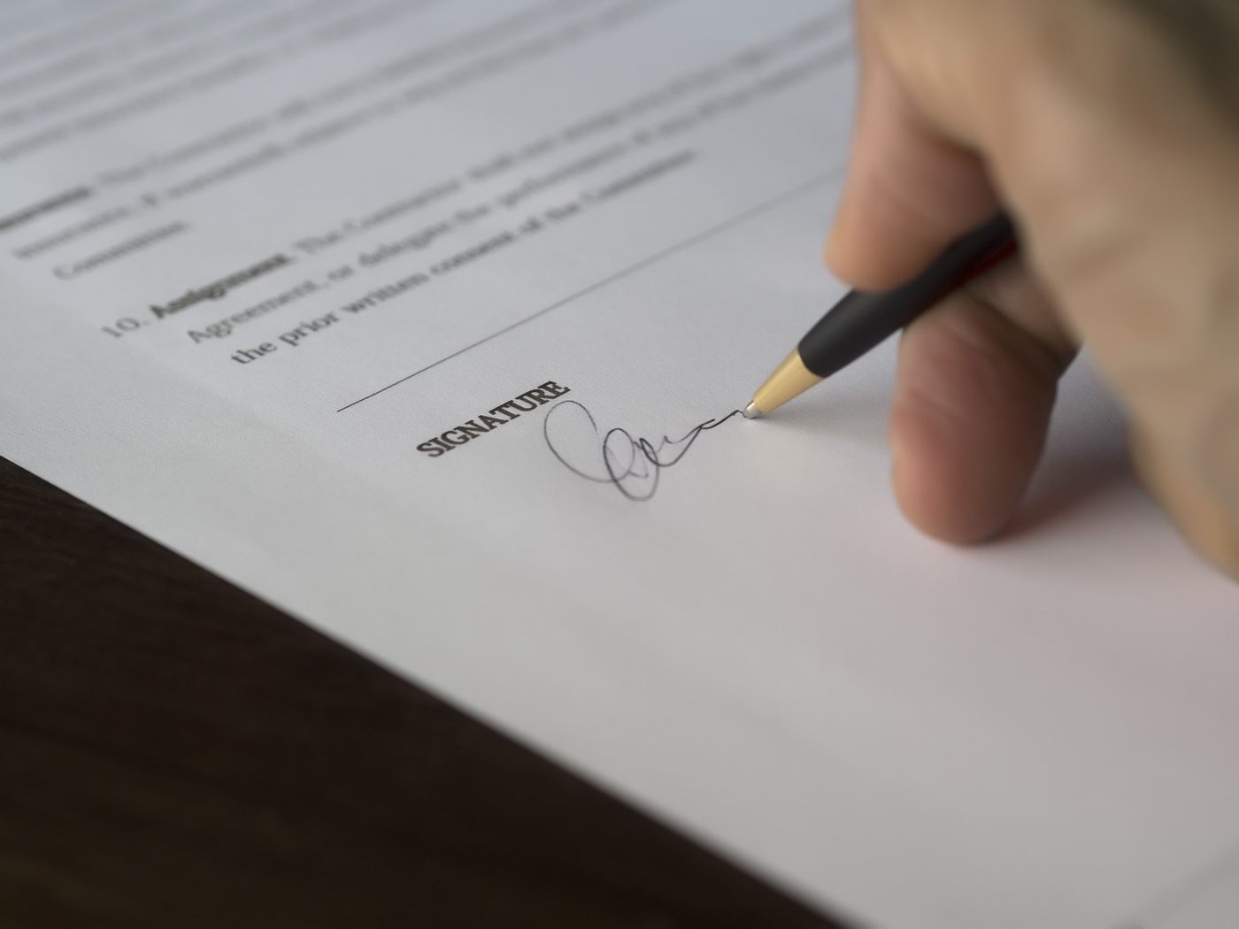 Close-up of a hand signing a formal contract with a pen at a desk