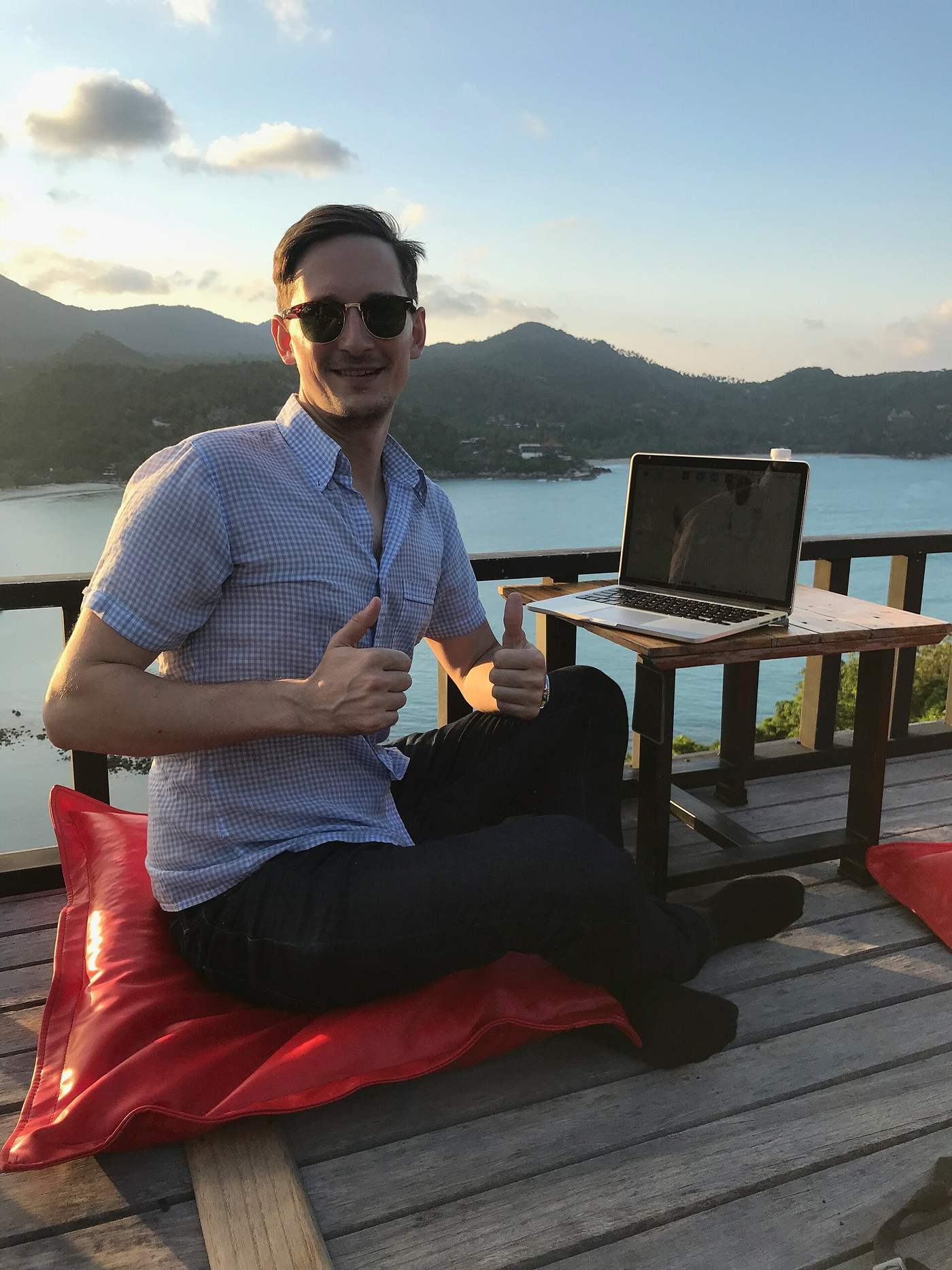 Digital nomad working on a laptop at a terrace table above a tropical bay