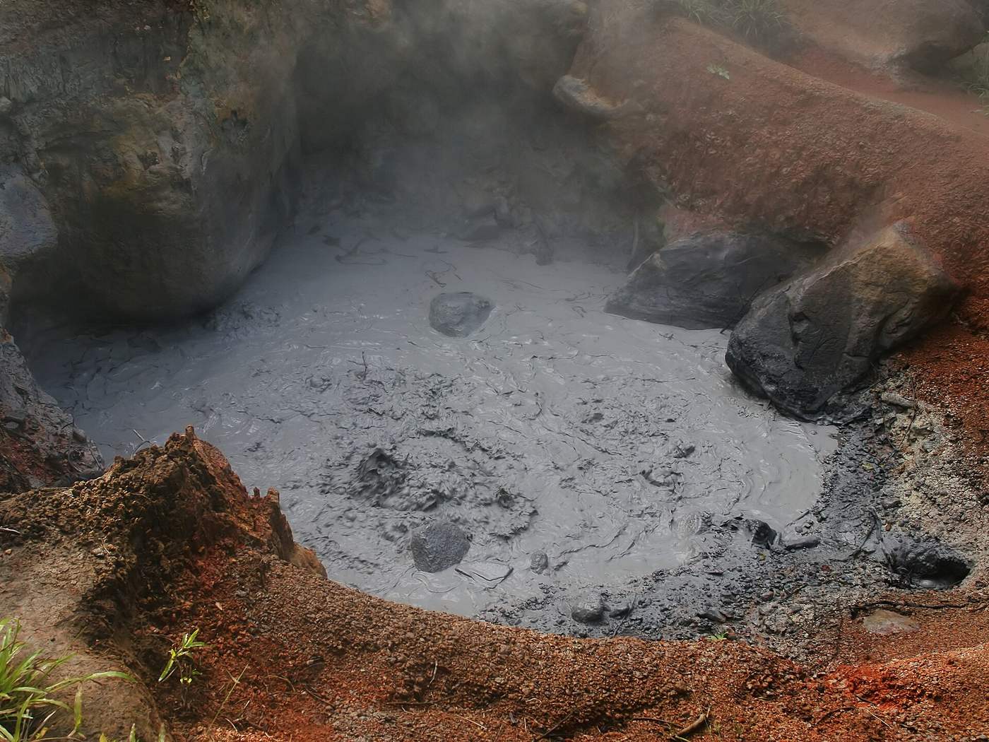 Steaming gray mud pot ringed by red volcanic rock at Rincon de la Vieja