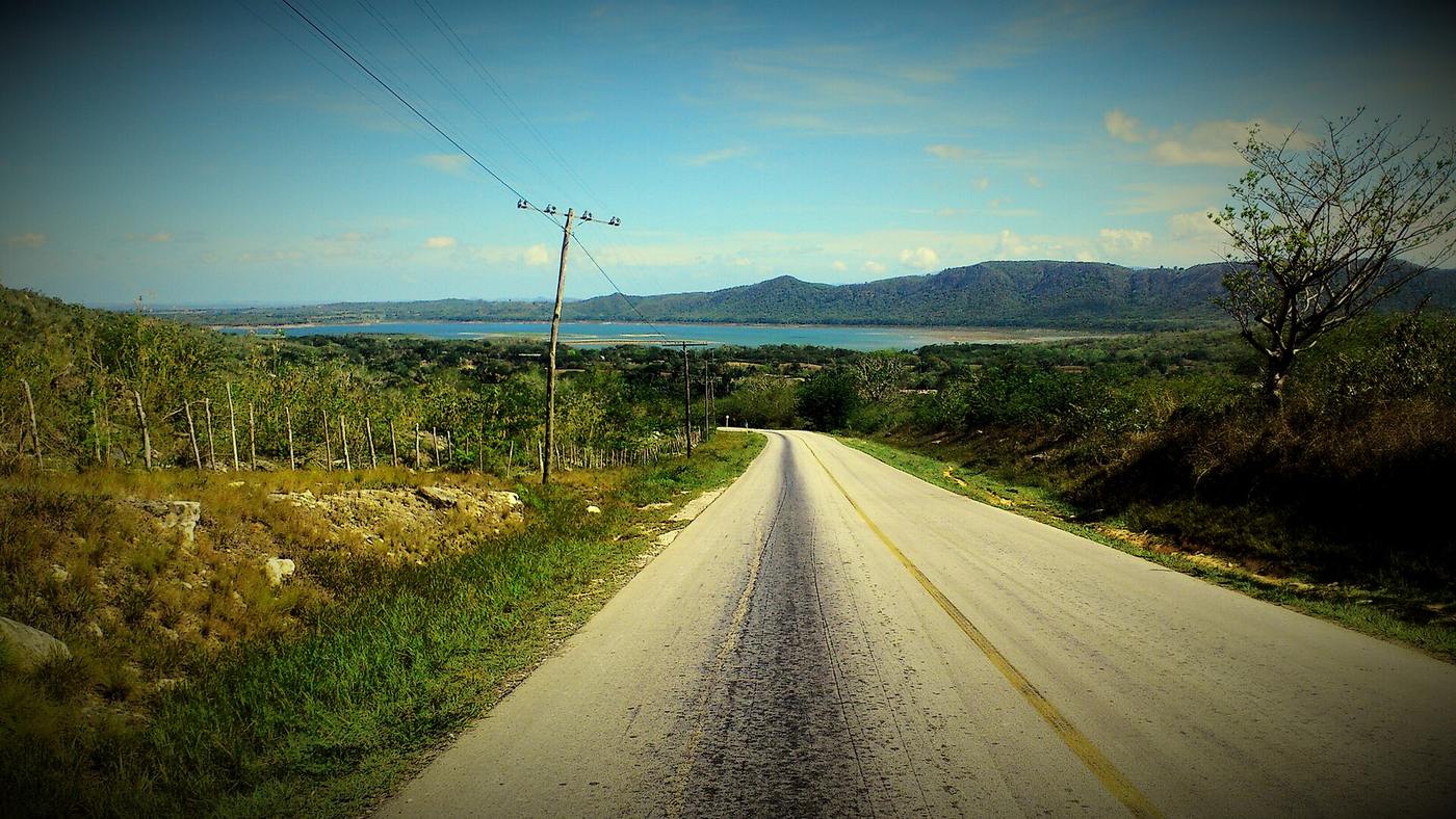 Empty two-lane road descending through dry Costa Rican hills toward a blue bay