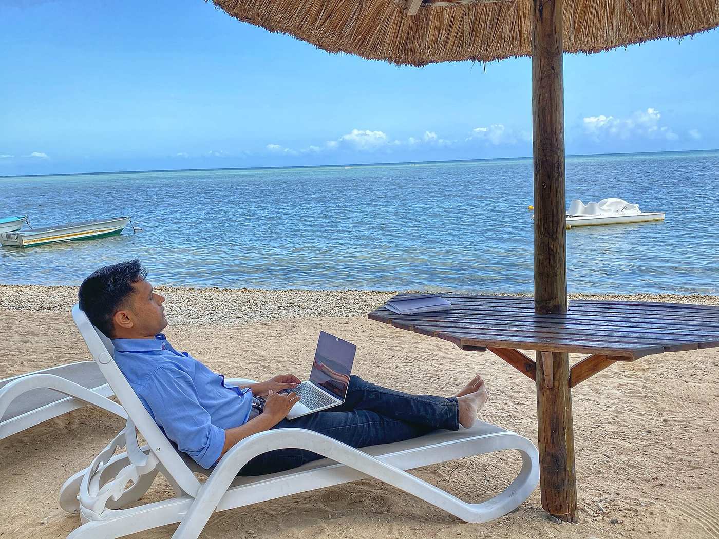 Remote worker typing on a laptop from a beach lounger under a palapa