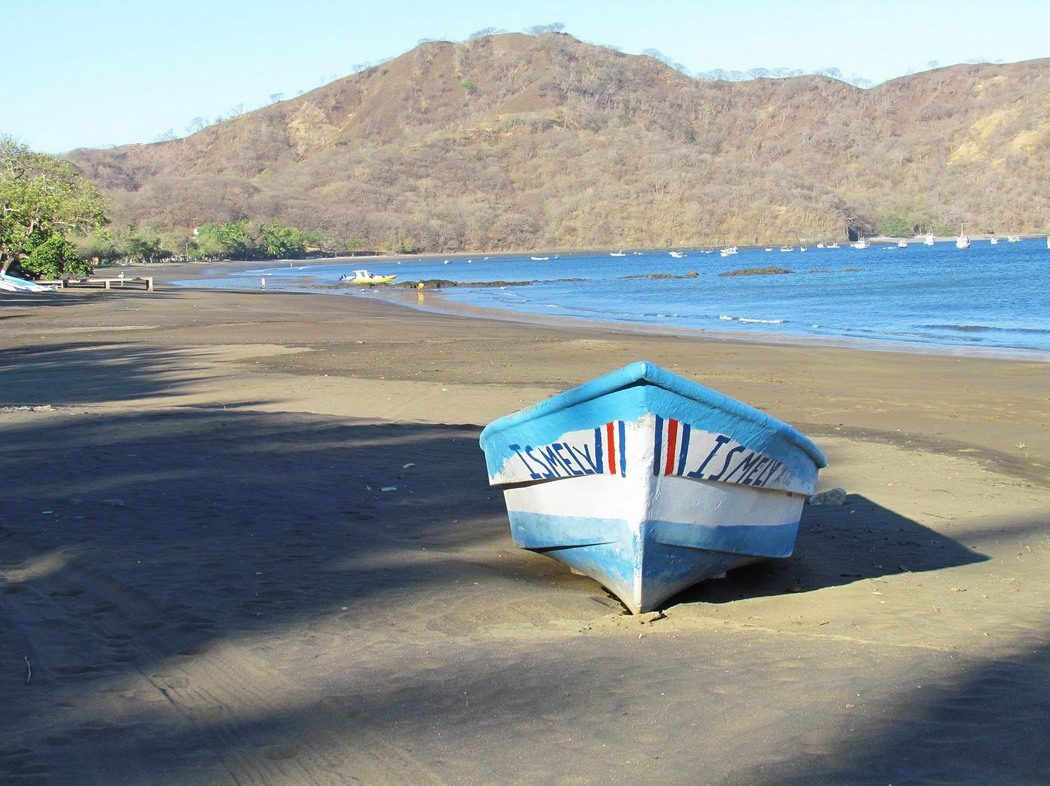 Painted fishing boat on Playas del Coco beach with bay and hills behind