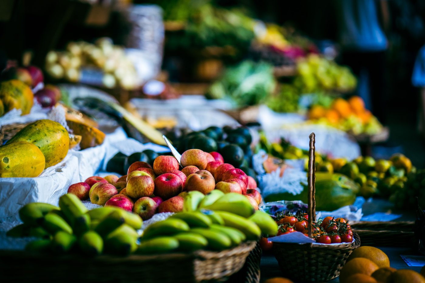 Farmers market stall piled with papaya, bananas, apples, and cherry tomatoes