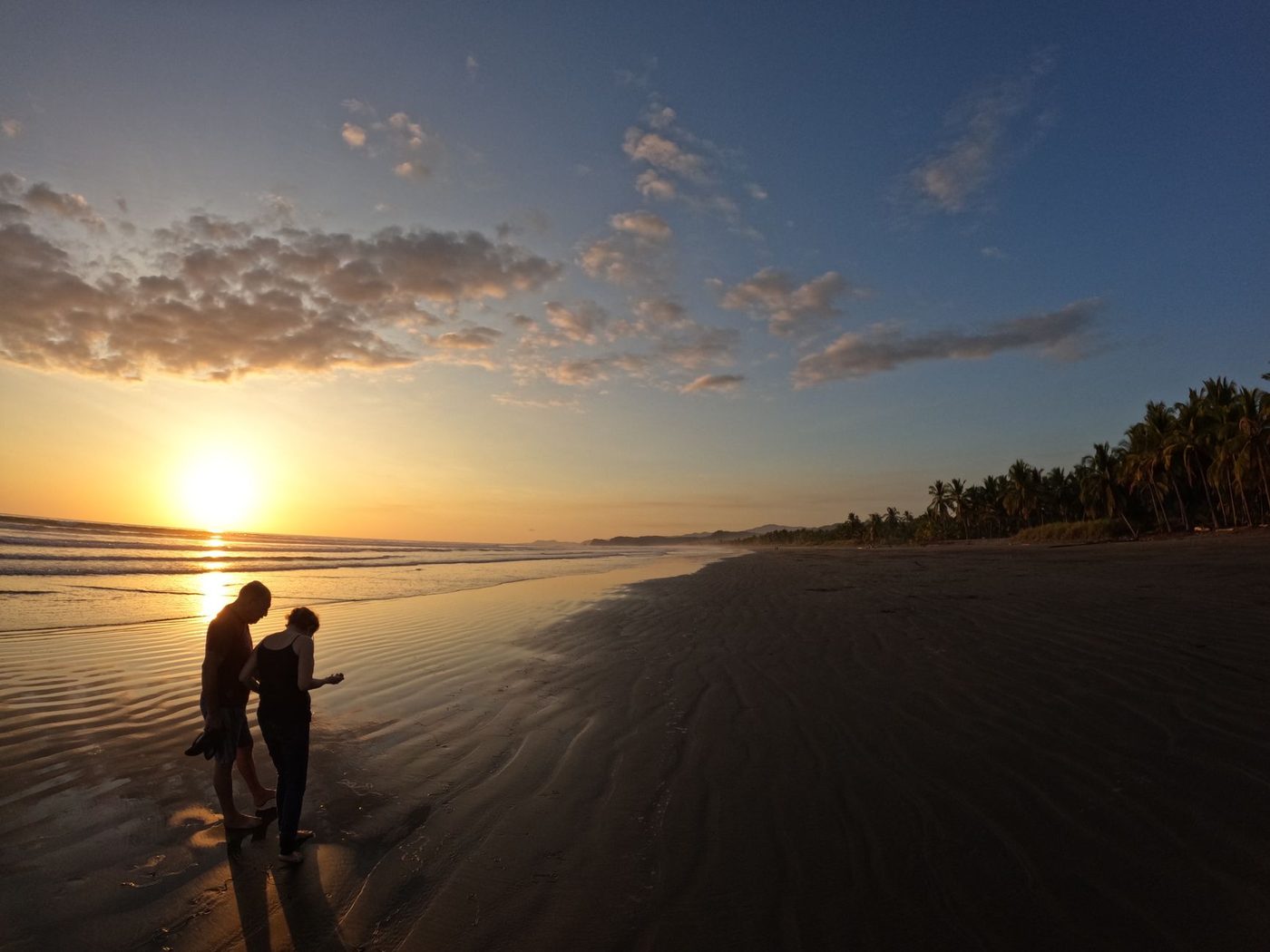Two silhouetted figures walking a quiet Guanacaste beach at golden sunset