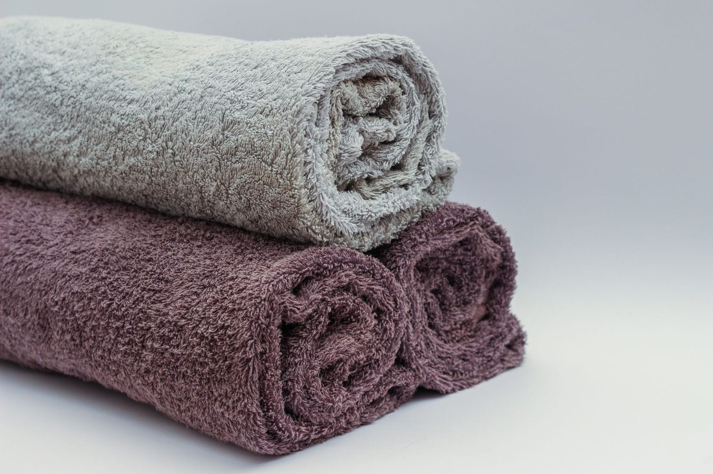Neatly rolled bath towels in neutral tones stacked on a light surface