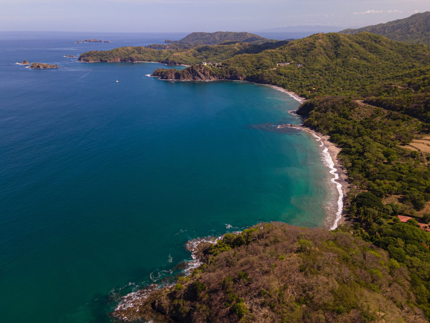 Aerial view of a forested Guanacaste bay and coastline with turquoise water and rocky headlands