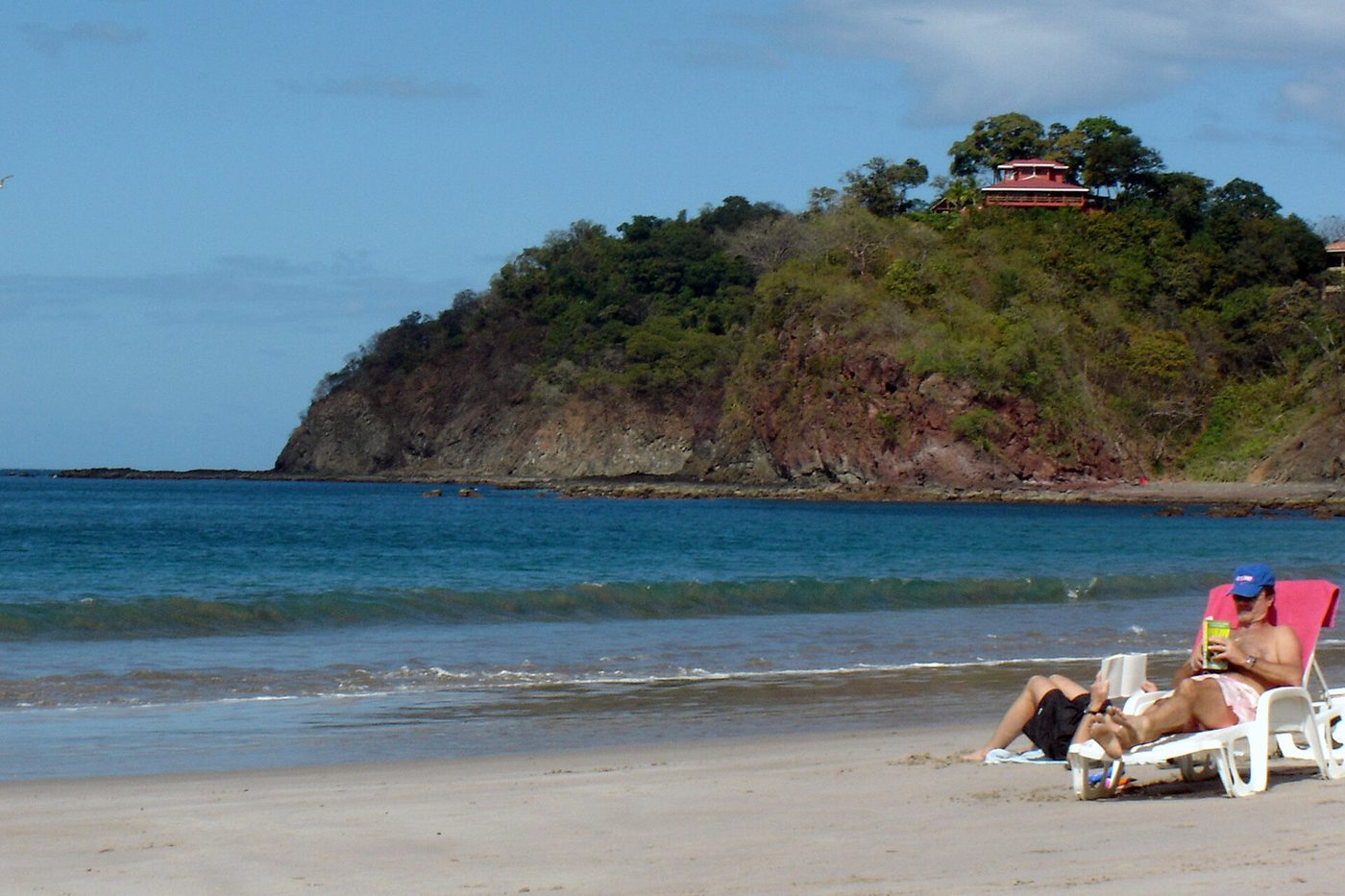 Vacationers relax on beach loungers below a hillside villa on Guanacaste's Gold Coast