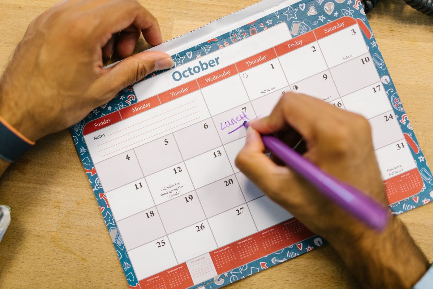 Hands marking reservation dates on an October wall calendar with a purple pen