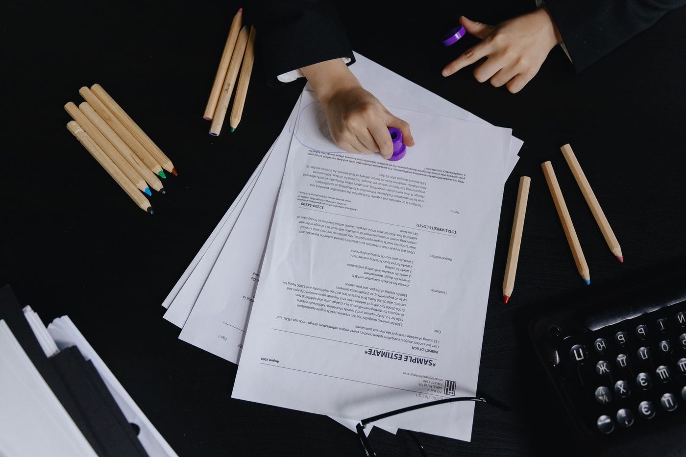 Hands stamping a corporate document on a desk with pencils nearby