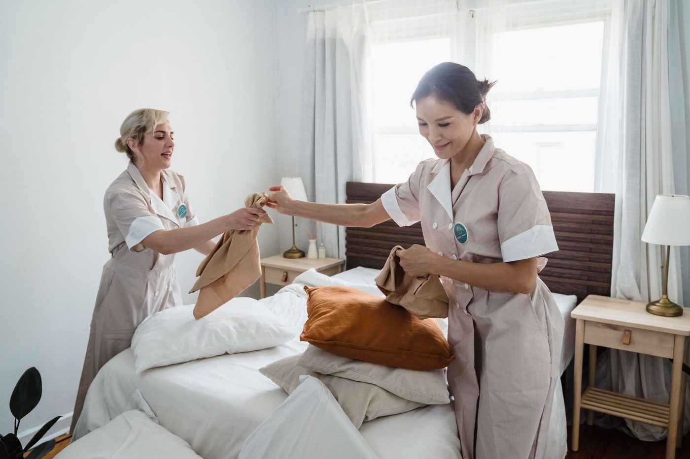 Two uniformed housekeepers changing bed sheets during a vacation rental turnover