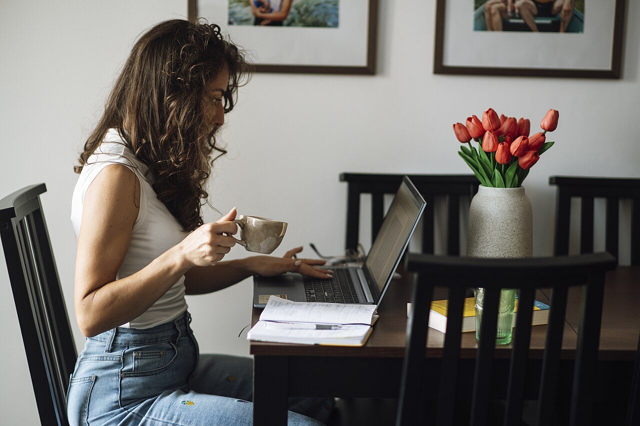 Woman drinking coffee while working on a laptop at a home office table