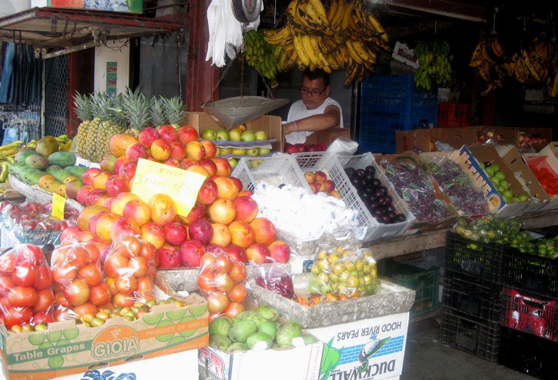 Vendor's stall piled with mangoes, pineapples, and bananas at a Costa Rican fruit market
