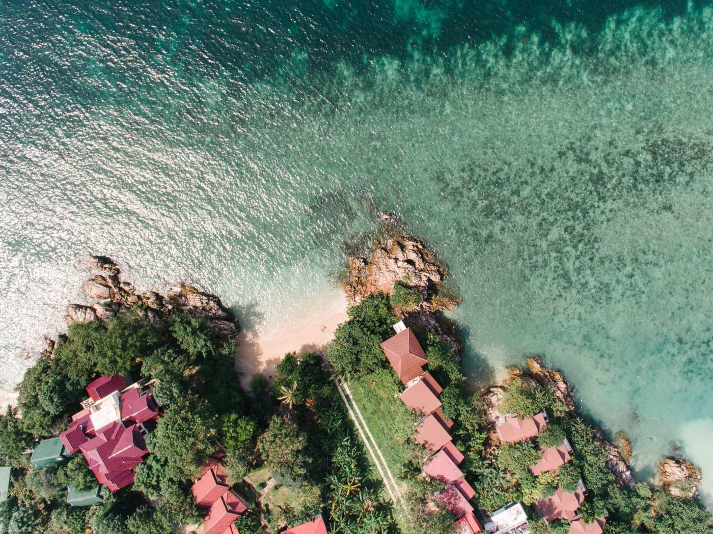 Red-roofed homes tucked into coastal greenery above a clear turquoise cove