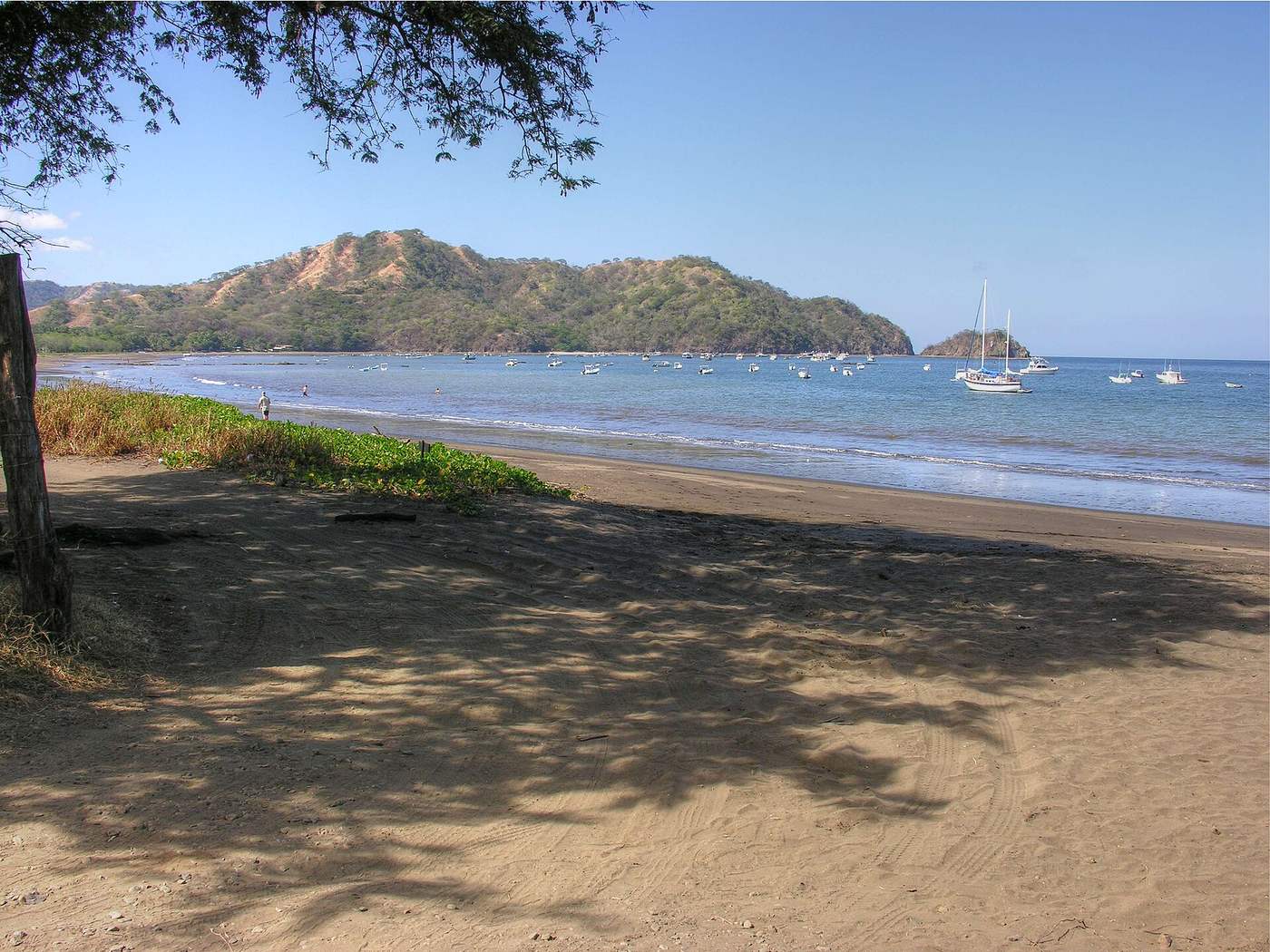 Shaded dark sand beach at Playas del Coco with boats anchored in the bay
