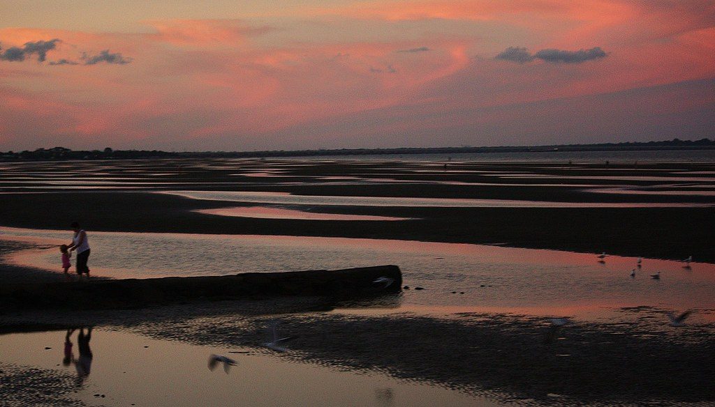 A mother and small child walking the shoreline at sunset