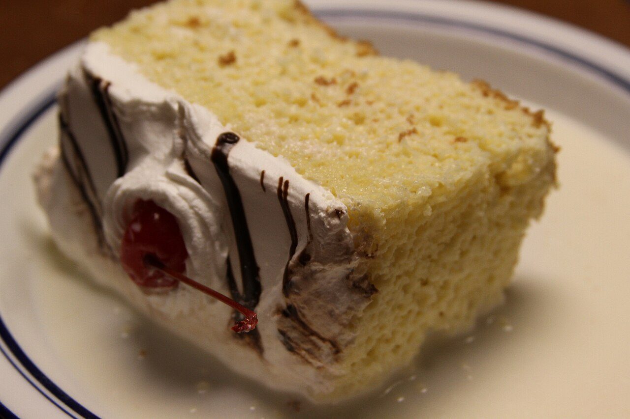 Slice of tres leches cake with whipped cream and a maraschino cherry