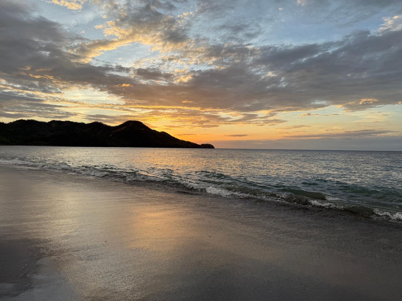 Golden sunset over a calm Guanacaste beach with gentle waves and a headland