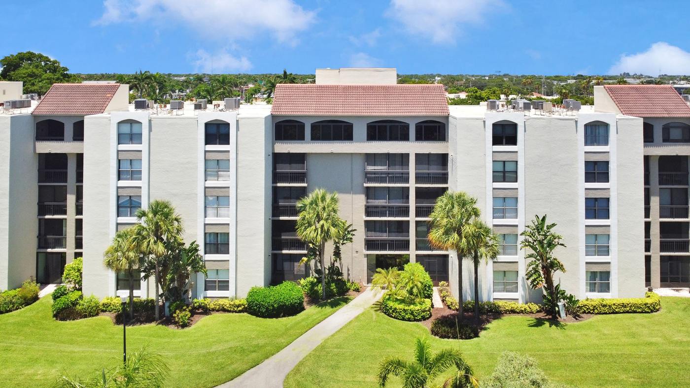 White multi-story condominium building with palm trees and a manicured green lawn