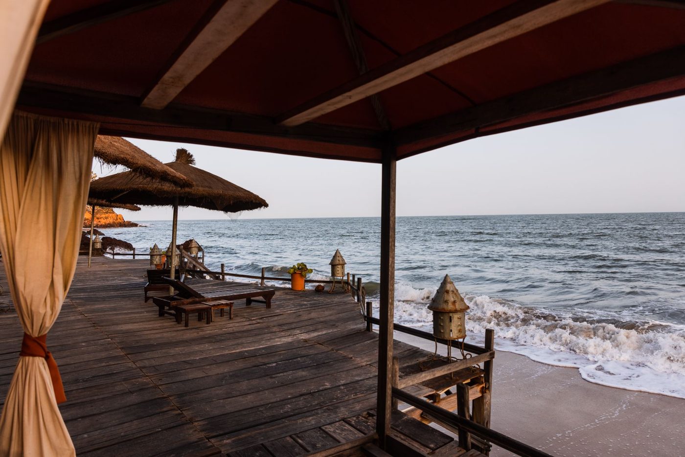 Peaceful wooden beach terrace with thatched umbrellas overlooking calm ocean waves