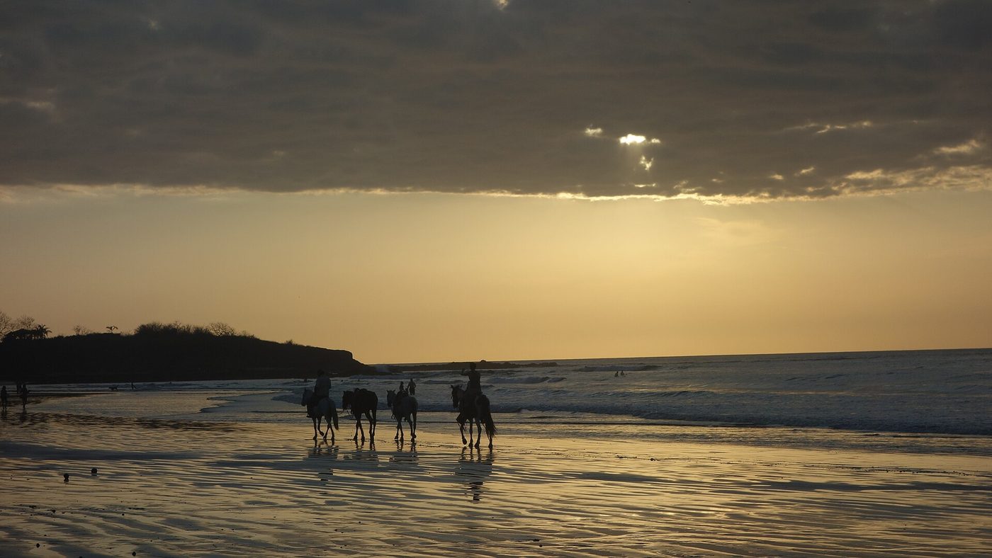 Horseback riders crossing Playa Tamarindo at sunset in Guanacaste, Costa Rica