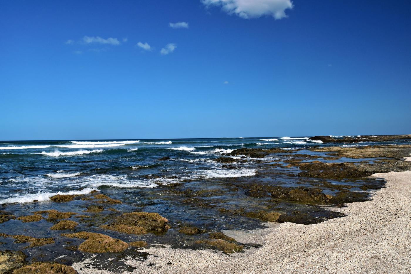 Rocky tide pools and breaking waves along Tamarindo's shoreline on a clear day