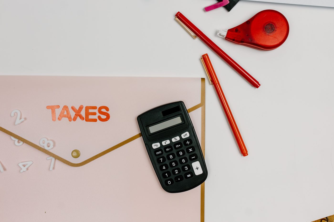 Flat lay of a taxes folder with a calculator, pens, and number stickers