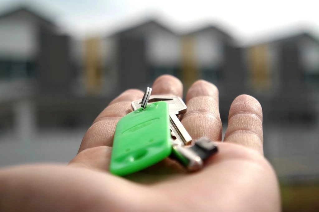 Hand holding house keys with a row of new homes blurred behind