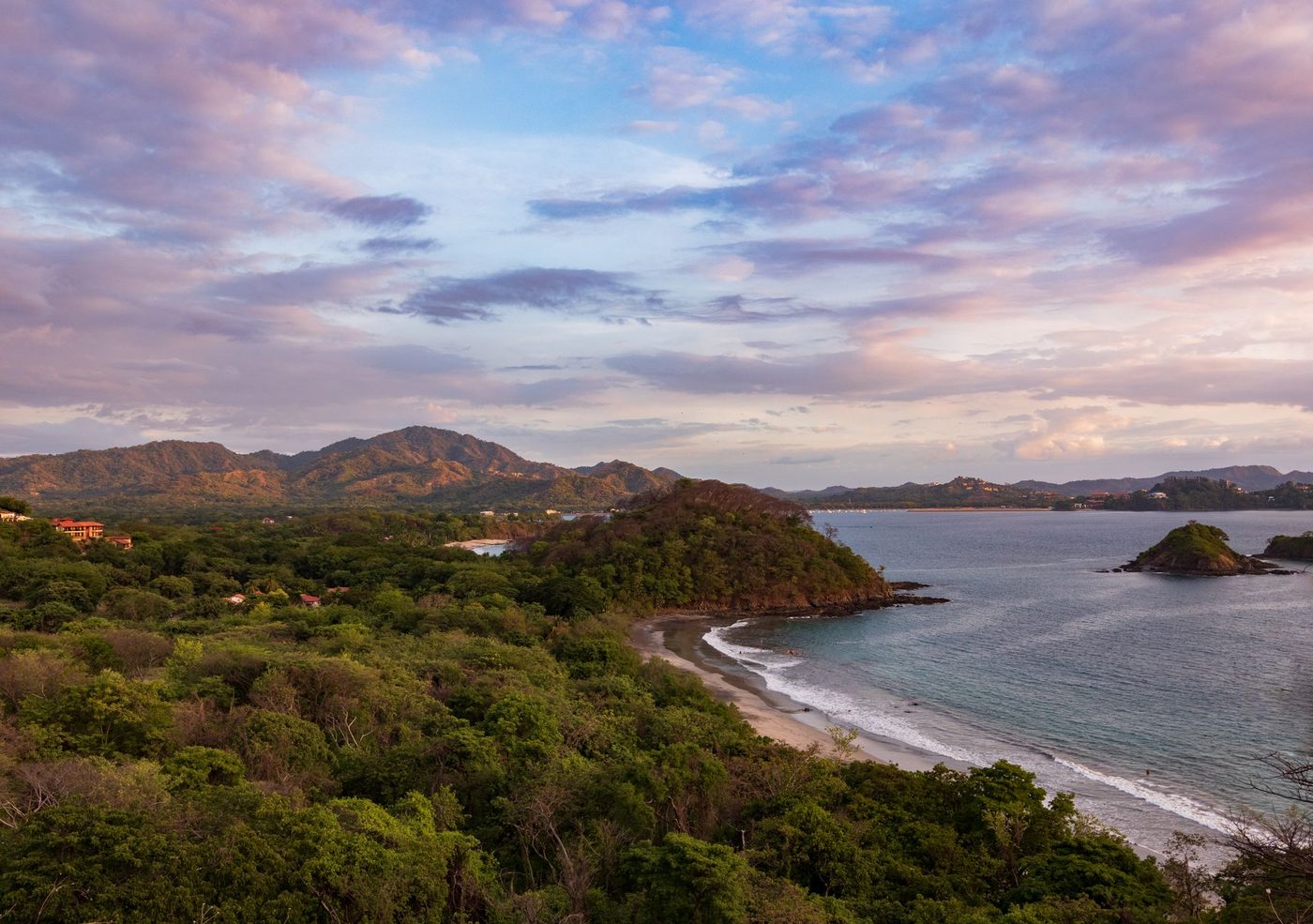Aerial view of a Guanacaste coastal town and bay under a pastel sunset sky