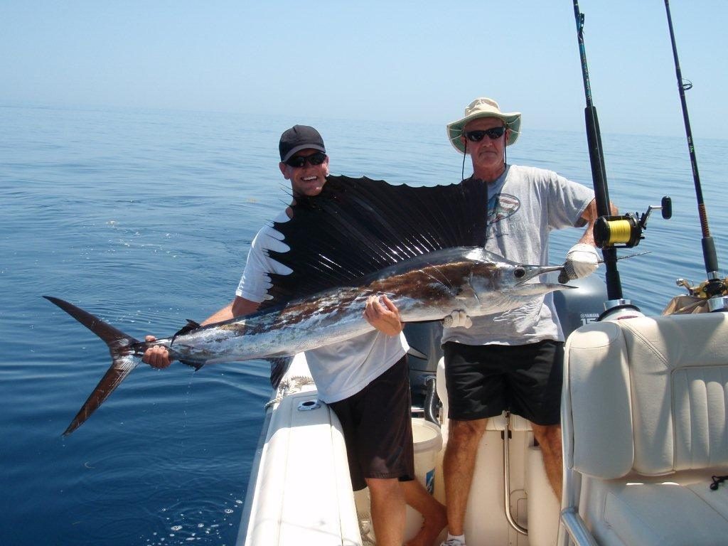 Two anglers holding a Pacific sailfish beside their charter boat before release