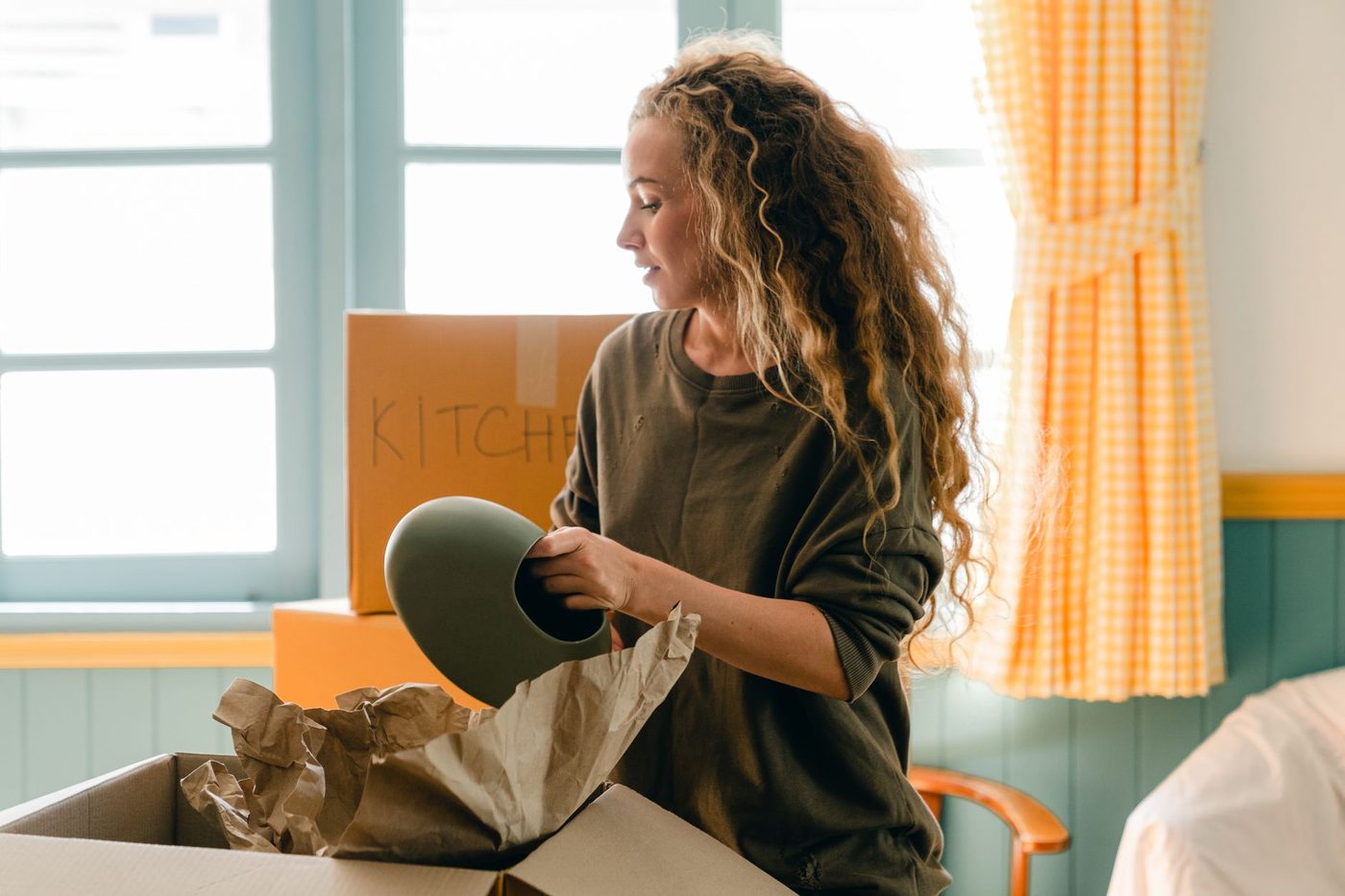 Woman unpacking a ceramic vase from a labeled kitchen moving box in bright room