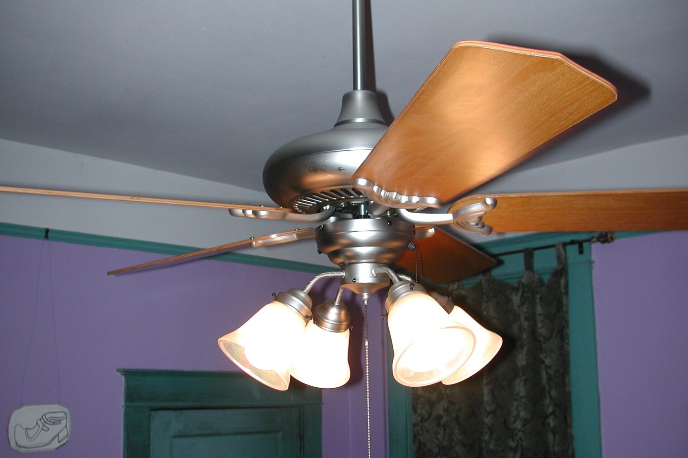 Ceiling fan with wooden blades and light kit spinning on a bedroom ceiling