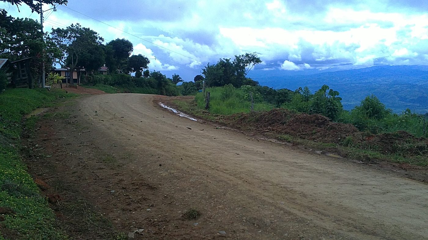 Dirt mountain road with muddy patches curving past rural Costa Rican homes