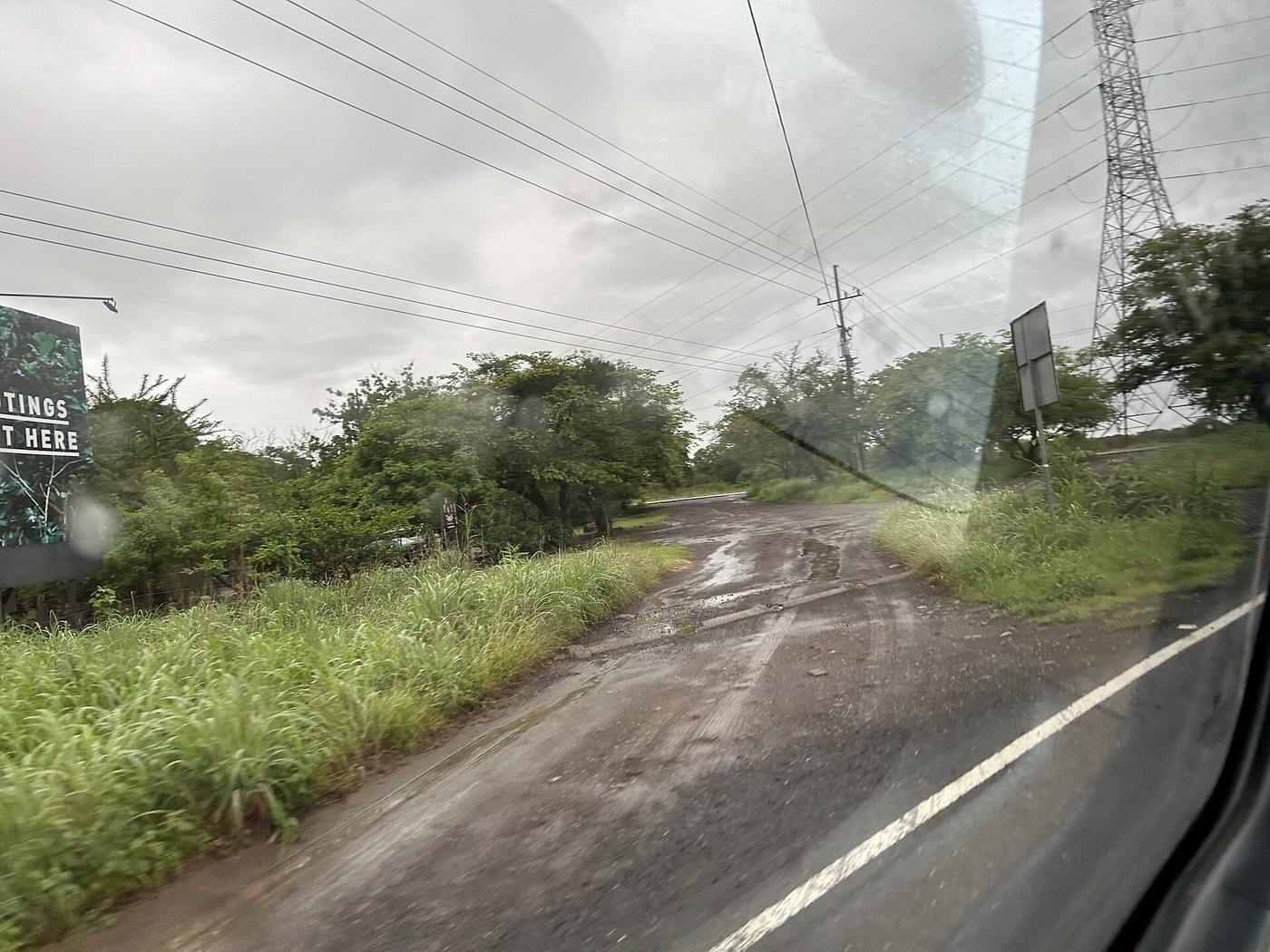 Muddy gravel side road branching off paved Route 253 in Guanacaste during rain