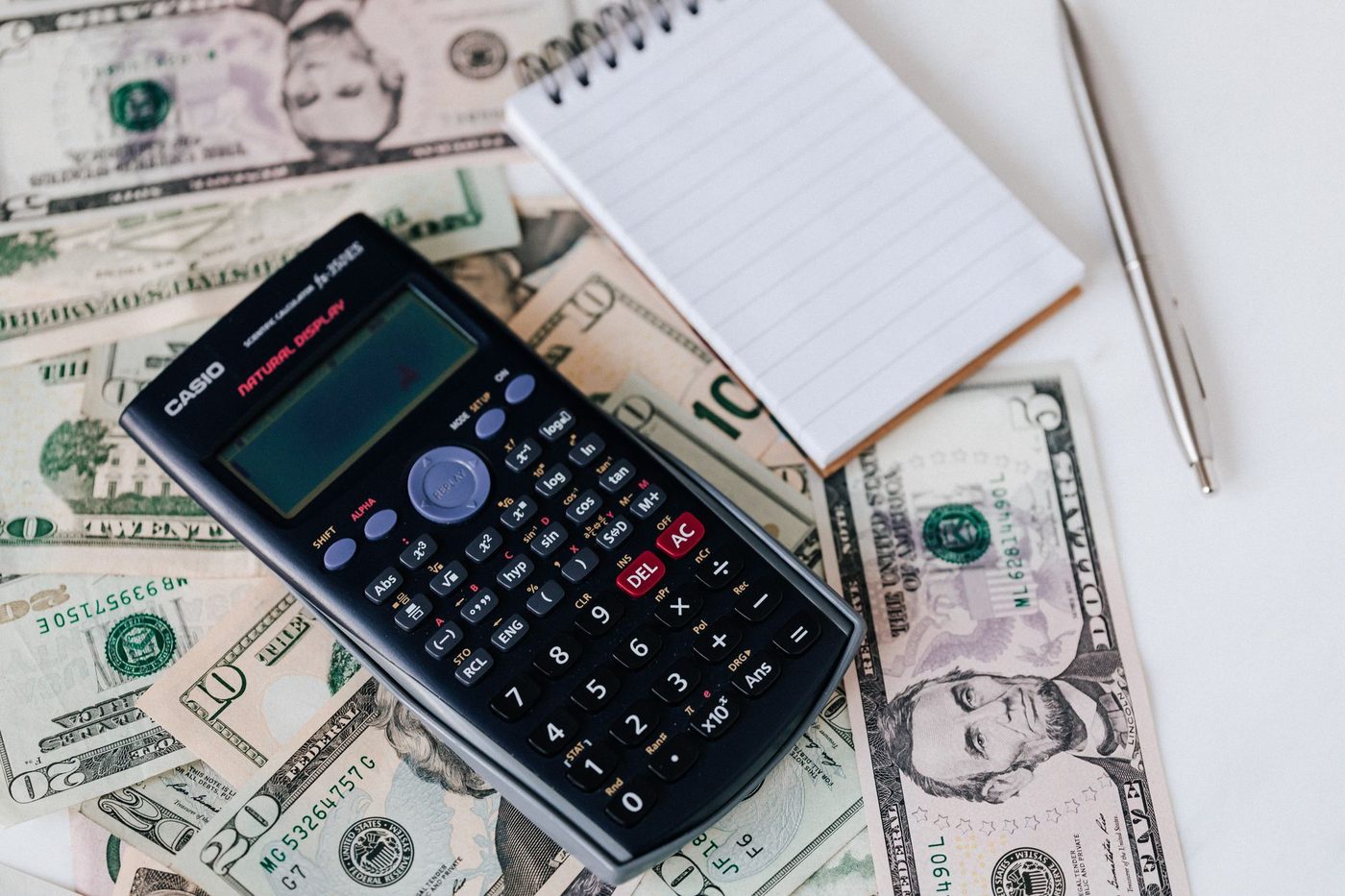 Calculator, notepad, and pen resting on a stack of US dollar bills