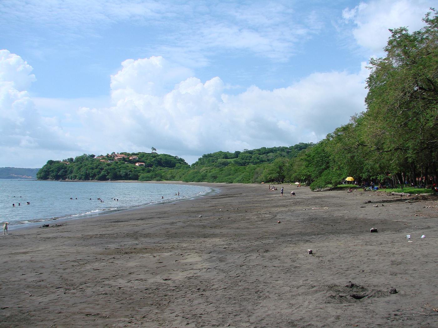 Swimmers and tree-lined dark sand beach at Playa Panama, Guanacaste