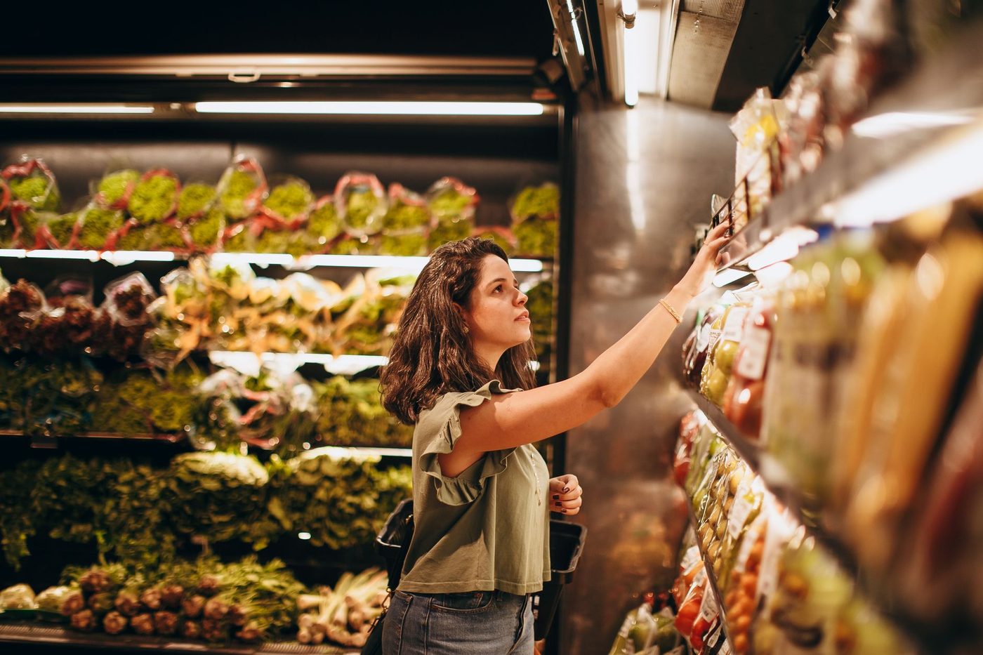Woman selecting fresh produce from a well-stocked grocery store vegetable aisle