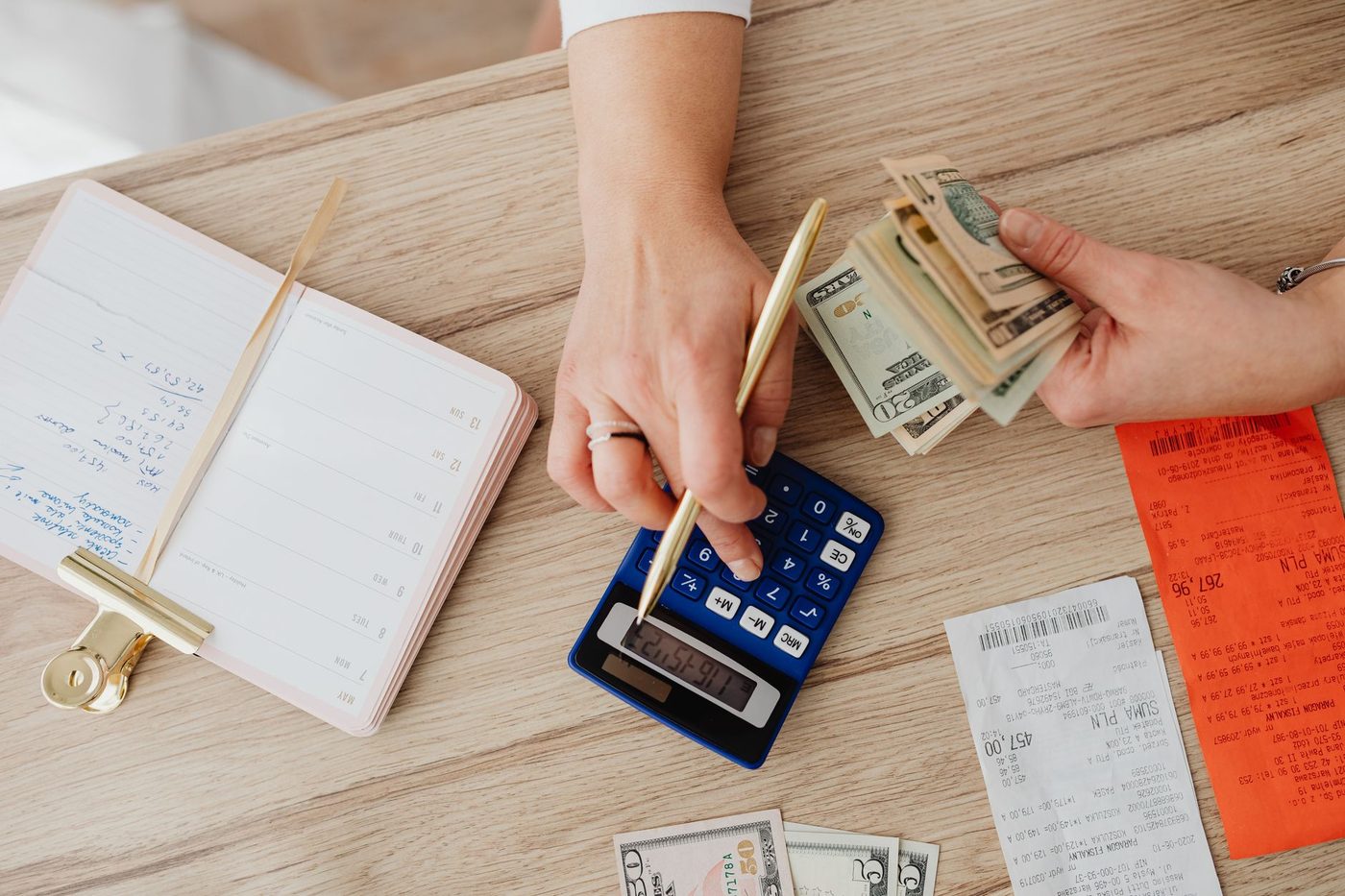 Hands using a calculator with cash and printed receipts to plan a monthly budget