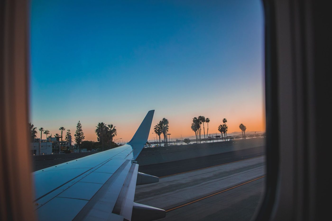 View from an airplane window of the wing and palm trees at sunset