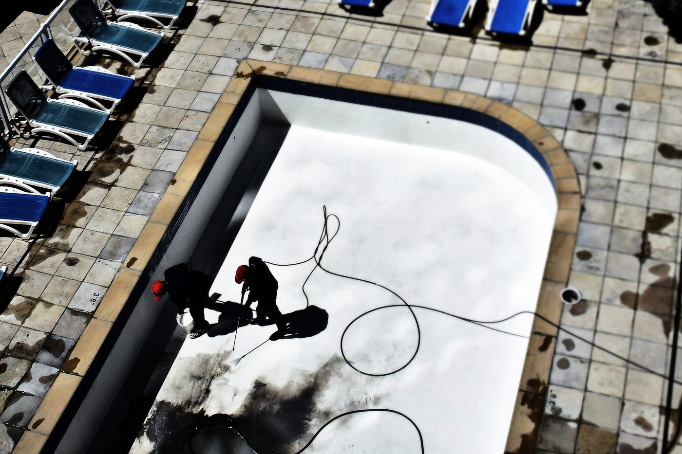 Two maintenance workers cleaning an empty swimming pool at a resort property