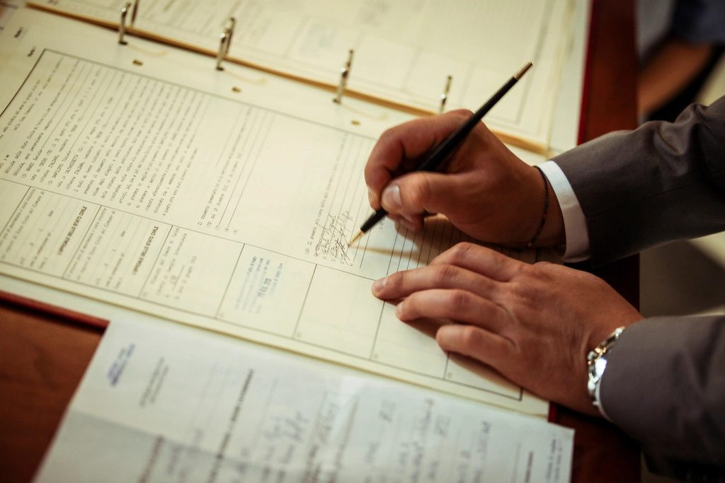 Man in gray suit signing an official document register with a pen