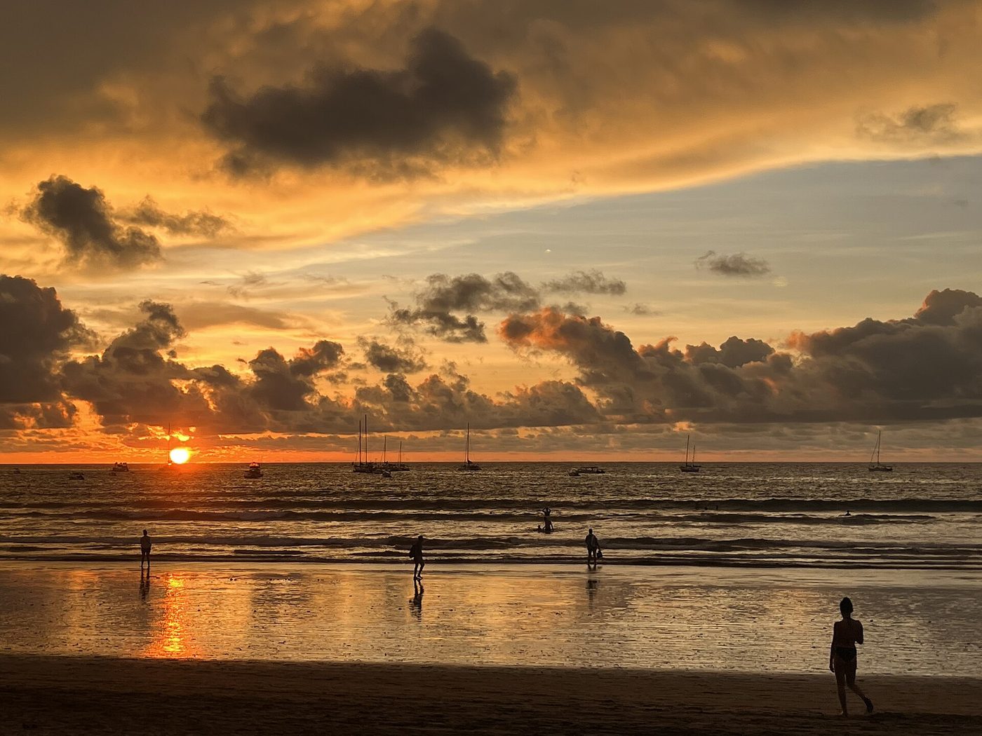 Golden sunset over a Guanacaste beach with sailboats anchored offshore and walkers silhouetted